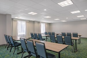 Un salón de conferencias con varias mesas y sillas, amplias ventanas con cortinas y suelo alfombrado.