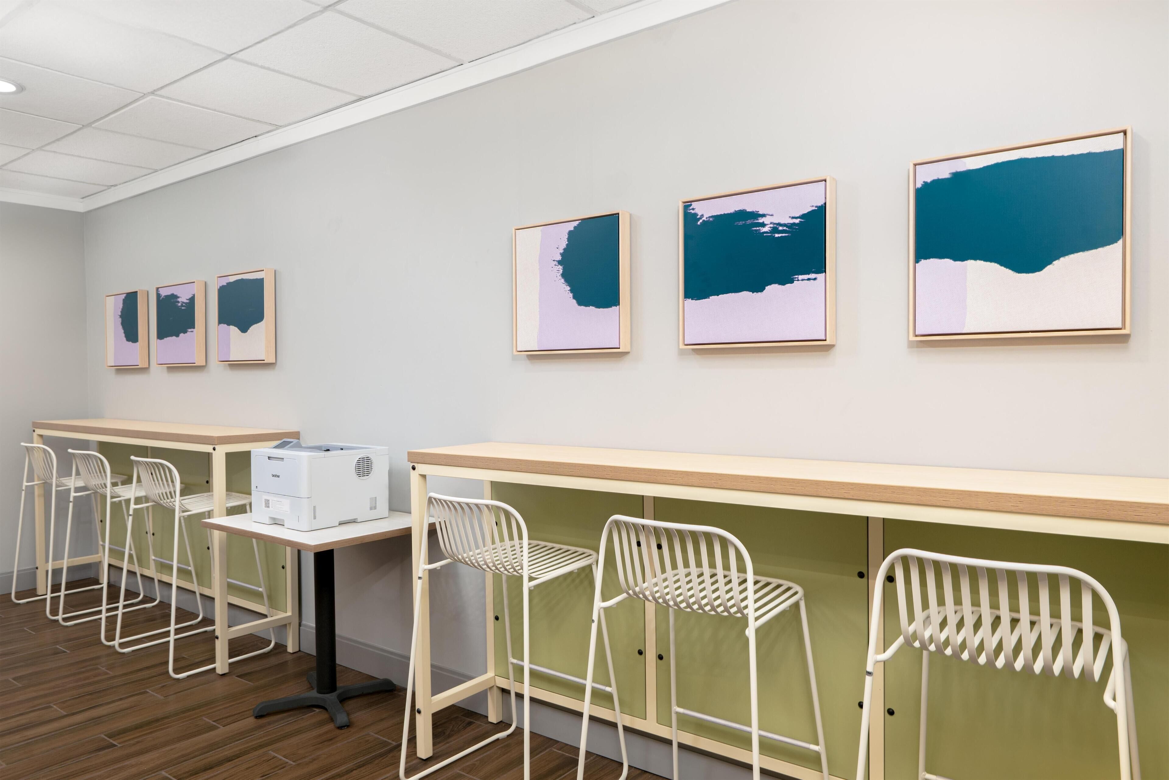 Une pièce avec une longue table, des chaises blanches et des œuvres d’art encadrées accrochées au mur.