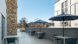 An outdoor patio area with stone walls, tables, chairs, and umbrellas. - Spark by Hilton Murfreesboro (Murfreesboro)