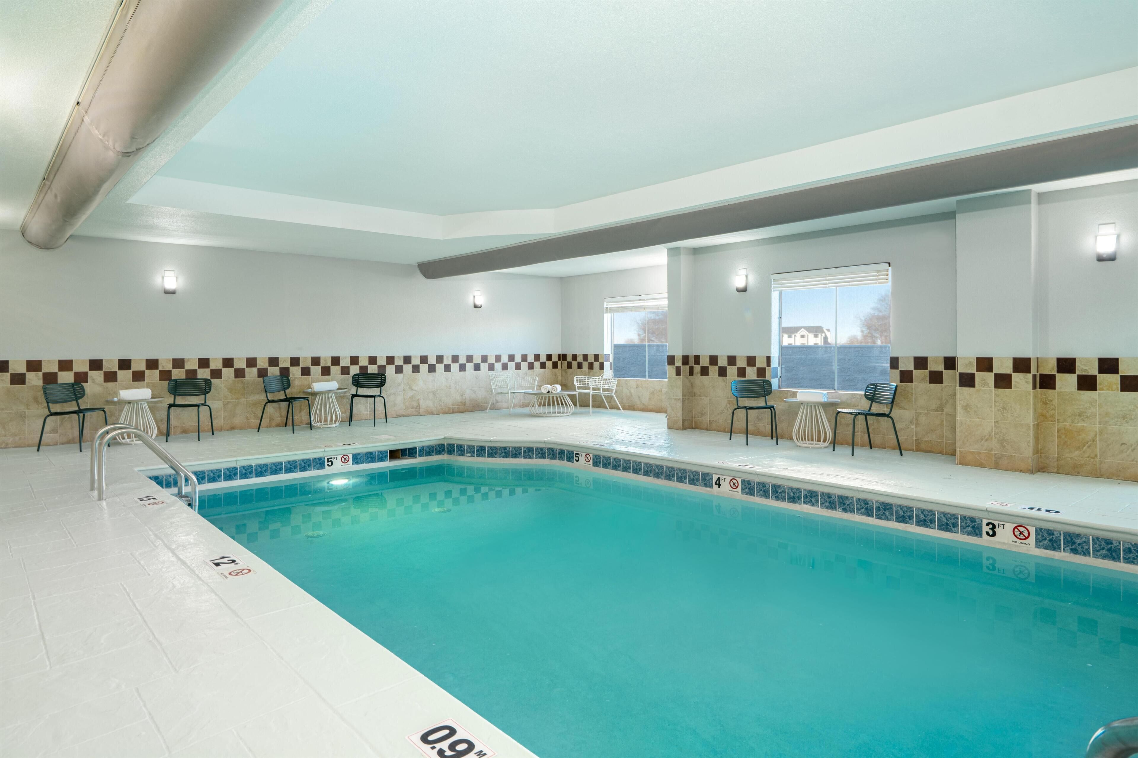 An indoor swimming pool with tiled walls, a checkered border, and lounge chairs.
