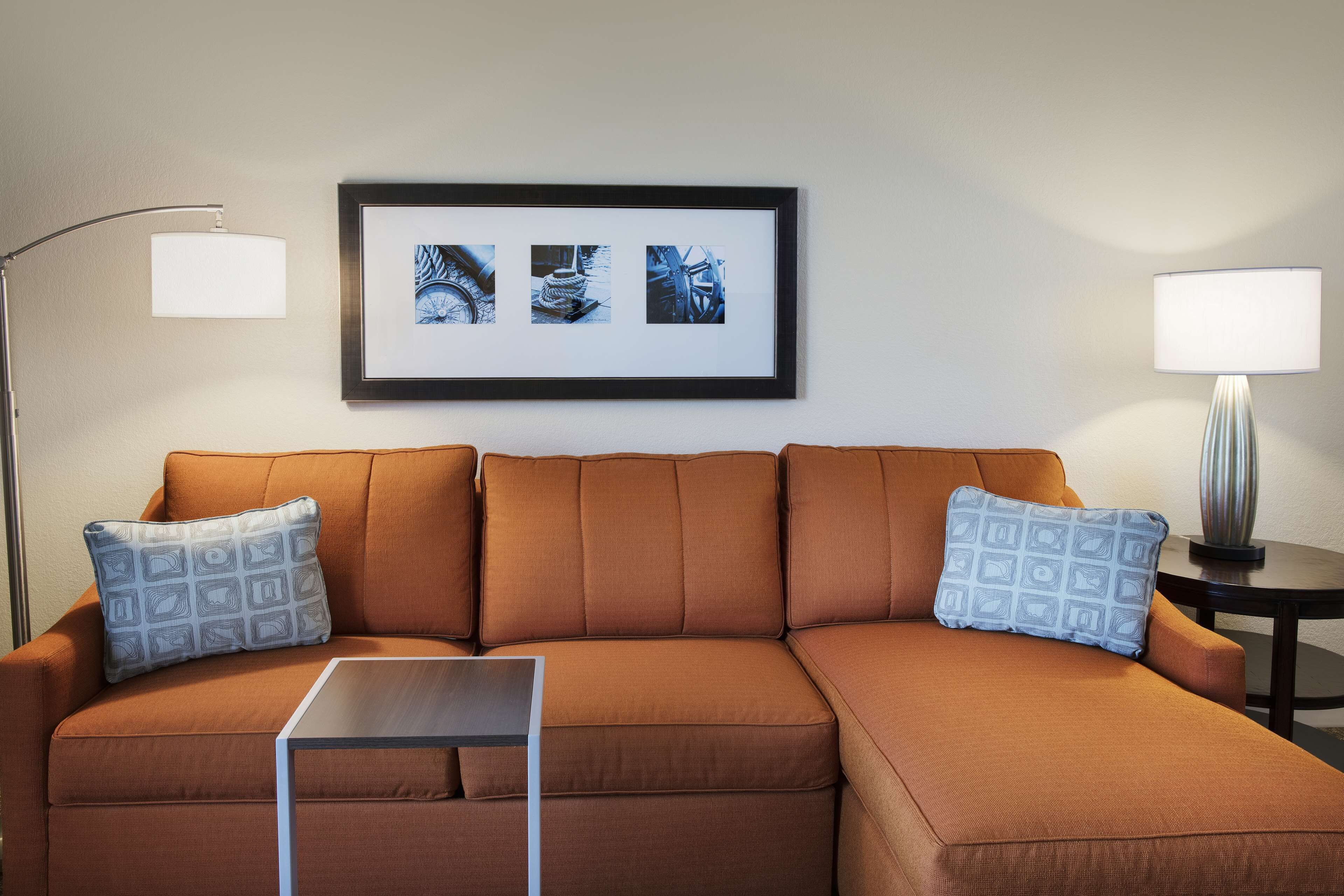 A modern living room with a brown sectional sofa, two patterned throw pillows, a small side table, and a framed picture on the wall.