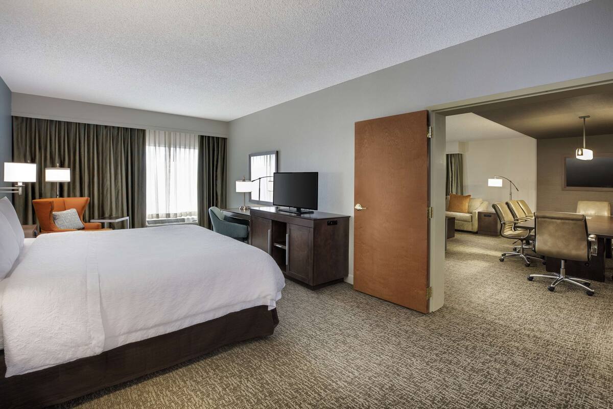 Une chambre d’hôtel dotée d’un grand lit, d’un bureau, d’une télévision et d’un coin salon séparé avec des fauteuils.