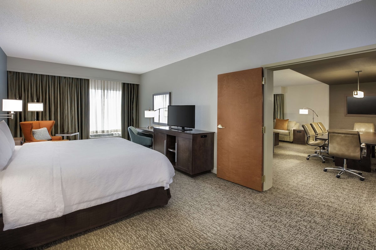 Ein Hotelzimmer mit einem großen Bett, einem Schreibtisch, einem Fernseher und einer separaten Sitzecke mit Stühlen.