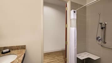 A bathroom with a sink, shower, and a small white shelf.