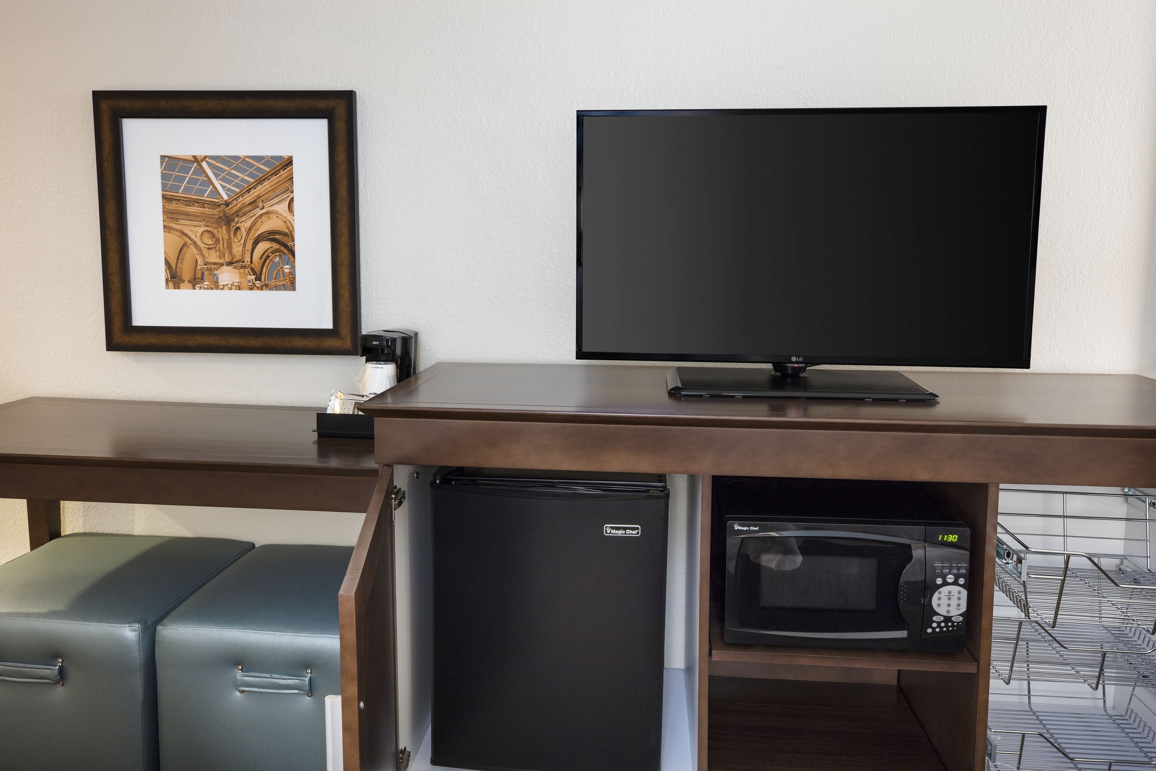 A room with a flat-screen TV, a refrigerator, a microwave, and a framed picture on the wall.