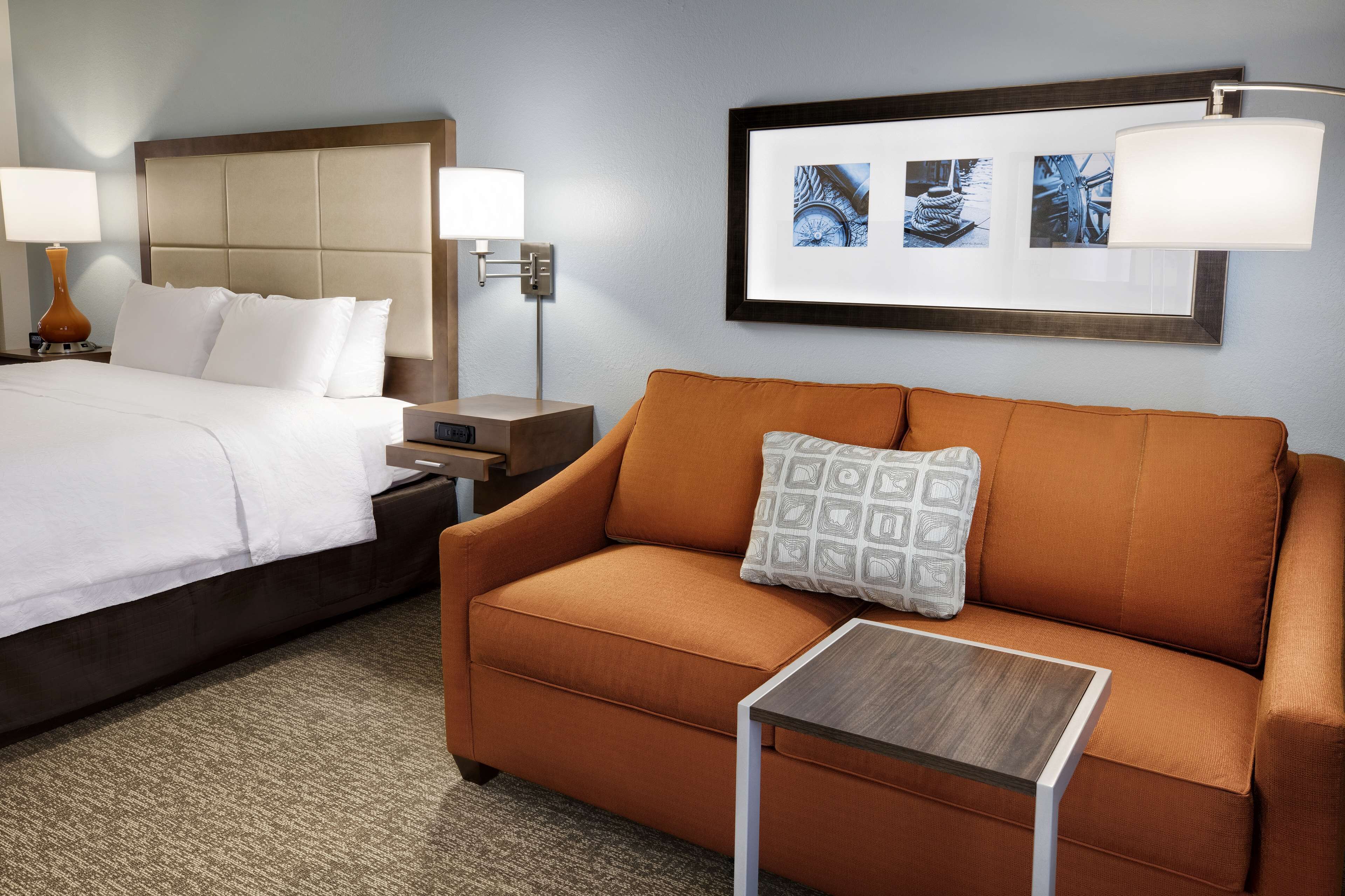 A hotel room with a bed, a sofa, a small table, and a nightstand.