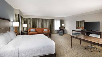 A hotel room with a large bed, a sofa, a desk, and a television.