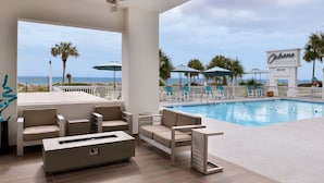Un espace aménagé au bord de la piscine, avec des meubles d’extérieur de couleur beige, une piscine et une vue sur la plage.