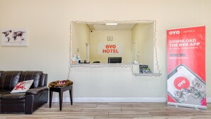 A reception area with a reception desk, a leather sofa, a small table with a flower arrangement, and a poster advertising the OYO app. - OYO Hotel Rosenberg TX I-69 (Rosenberg)