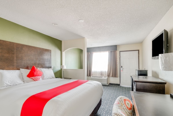 Quarto de hotel com uma cama grande, uma escrivaninha, uma televisão e uma porta.