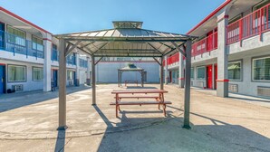 A covered outdoor area with a picnic table and a gazebo, surrounded by buildings with balconies and windows. - OYO Hotel Rosenberg TX I-69 (Rosenberg)
