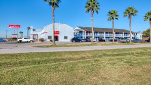 A motel with a white exterior, multiple balconies, and palm trees in front. - OYO Hotel Rosenberg TX I-69 (Rosenberg)