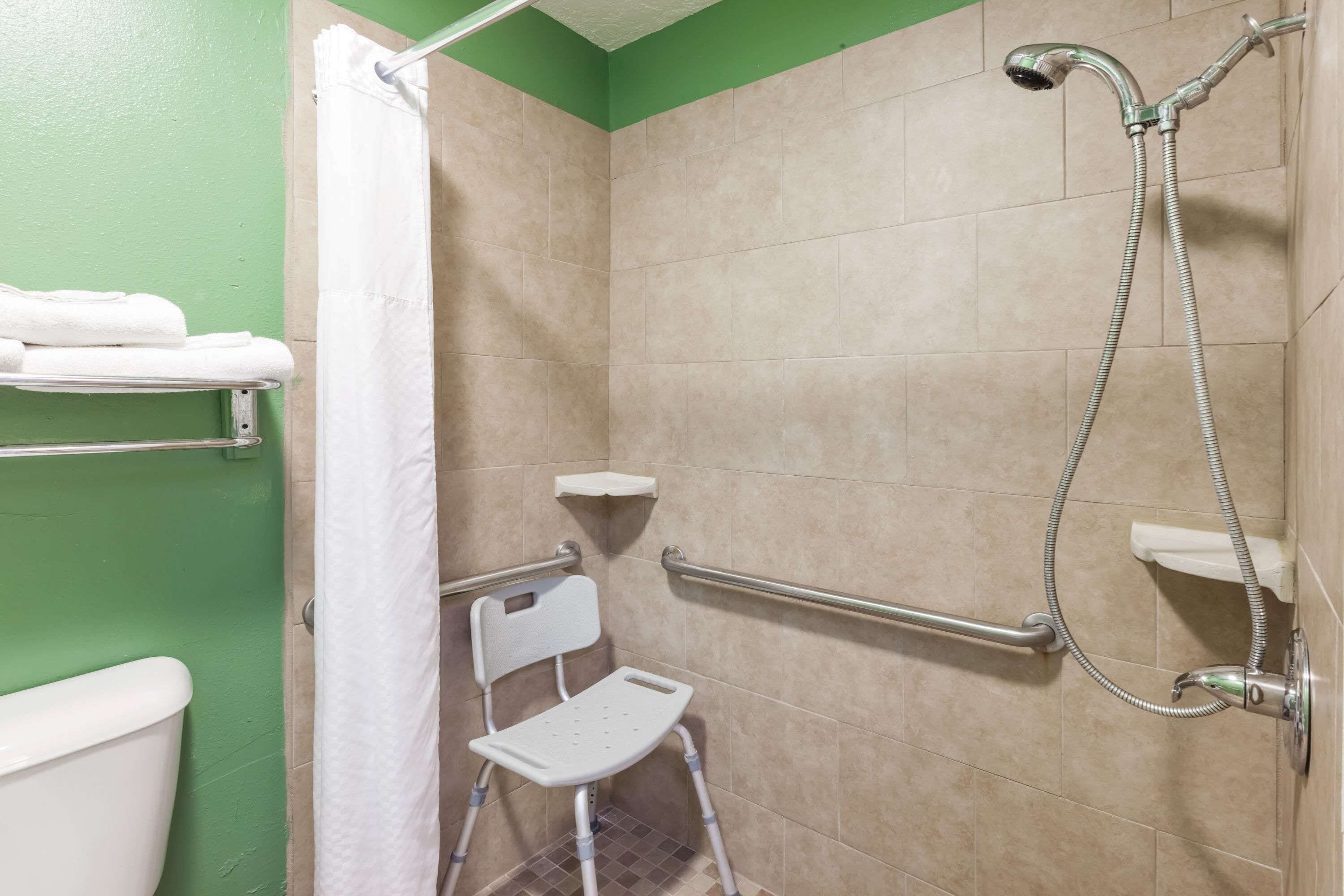 Baño con ducha, barras de apoyo, banco accesible en silla de ruedas y un inodoro.