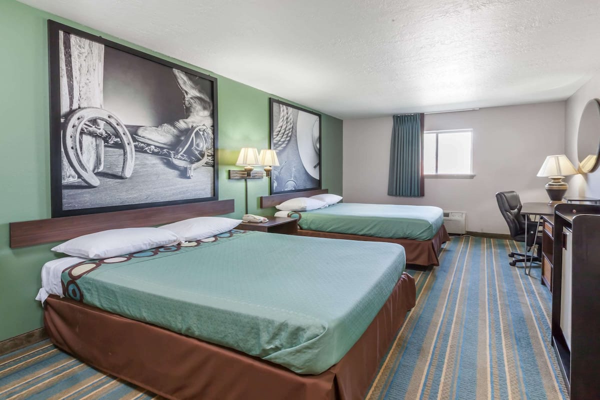 Une chambre d’hôtel avec deux lits, un bureau, une chaise et des œuvres d’art accrochées aux murs.