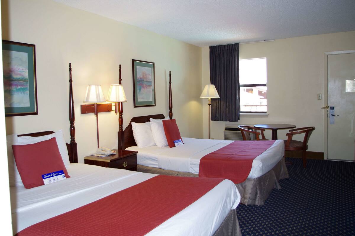 A hotel room with two beds, a desk, a chair, and a window with curtains.