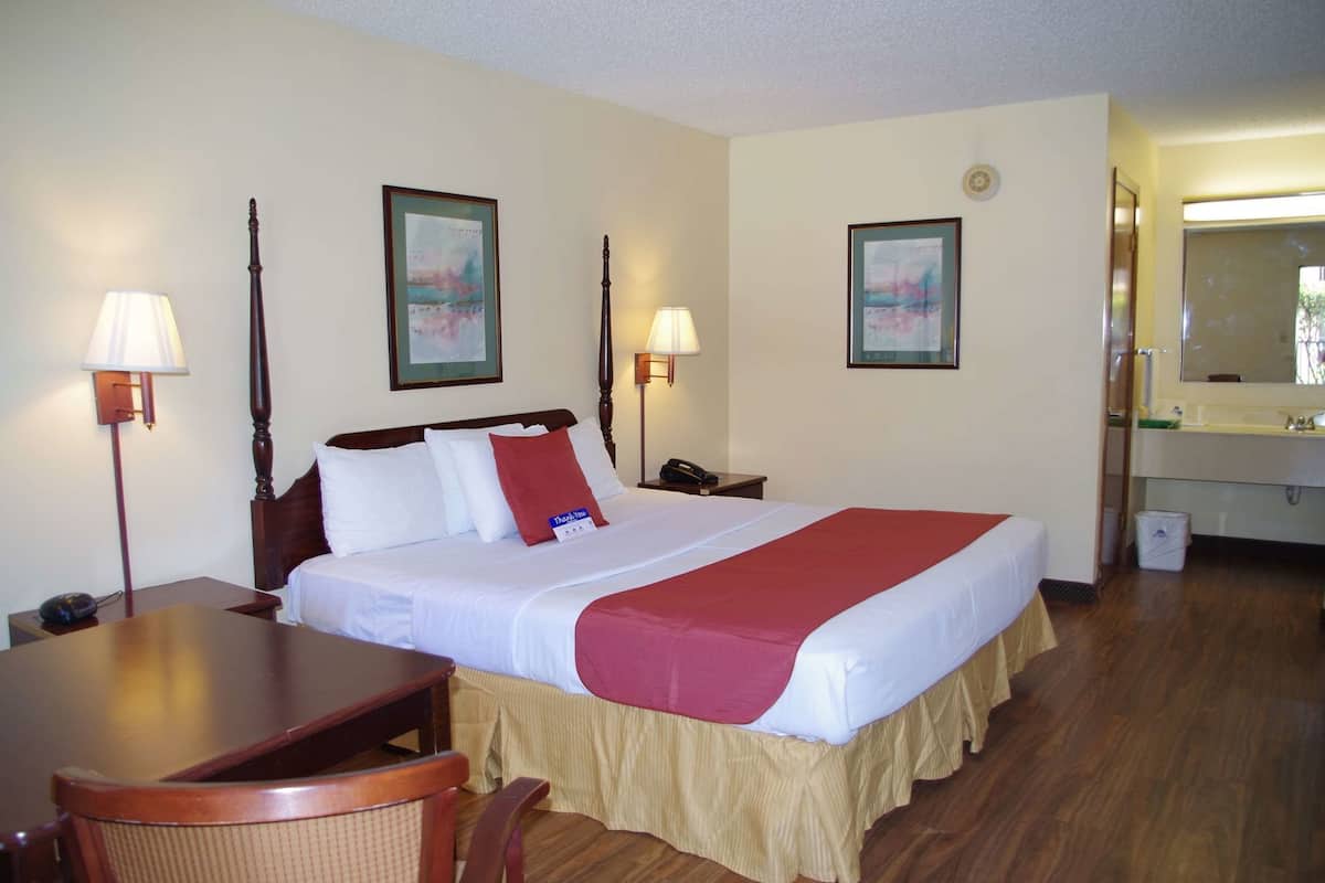 A hotel room with a bed, bedside lamps, a desk, a chair, a telephone, and a bathroom with a sink and mirror.