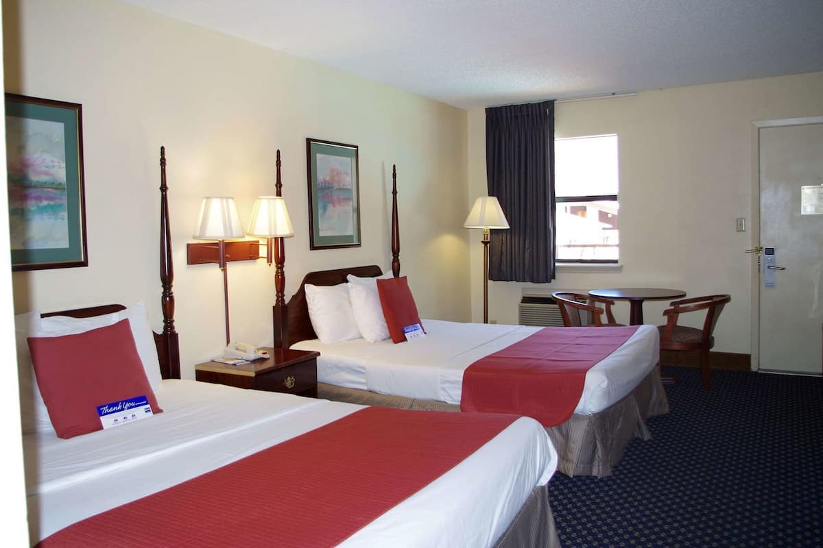 A hotel room with two beds, a desk, a chair, a window with curtains, and a door.