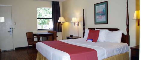 A hotel room with a large bed, a desk with a chair, a window with curtains, a painting on the wall, and two bedside lamps.