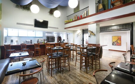 A spacious dining area with multiple tables and chairs, a kitchen in the background, and a balcony with plants.