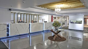 Un espace d’accueil moderne avec des comptoirs en marbre, un bureau d’accueil avec un plateau en verre et un plafond en bois.