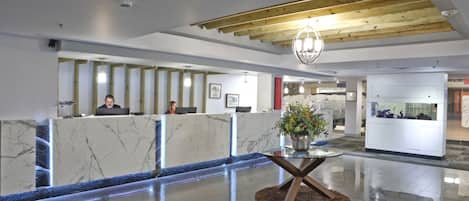 A modern reception area with marble counters, a glass-top reception desk, and a wooden ceiling.