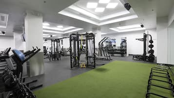Un gimnasio con diversos equipos de ejercicio, una zona de colchonetas verdes e iluminación empotrada en el techo.