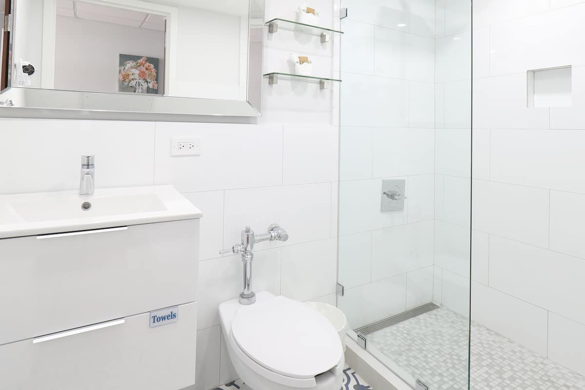 Un baño moderno con cabina de ducha de vidrio, un lavabo blanco y suelo estampado.