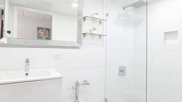 A modern bathroom with a glass shower enclosure, a white sink, and a patterned floor.