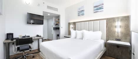 A modern hotel room with a large bed, a desk with a chair, a flat-screen TV, and a wooden accent wall.