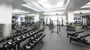 Une salle de sport avec des murs recouverts de miroirs, des supports à poids, des bancs et divers appareils d’exercice.