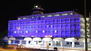 Un hôtel à plusieurs étages, reconnaissable à son grand panneau « HÔTEL » sur la façade, qui présente une architecture moderne avec un toit plat et de grandes fenêtres.