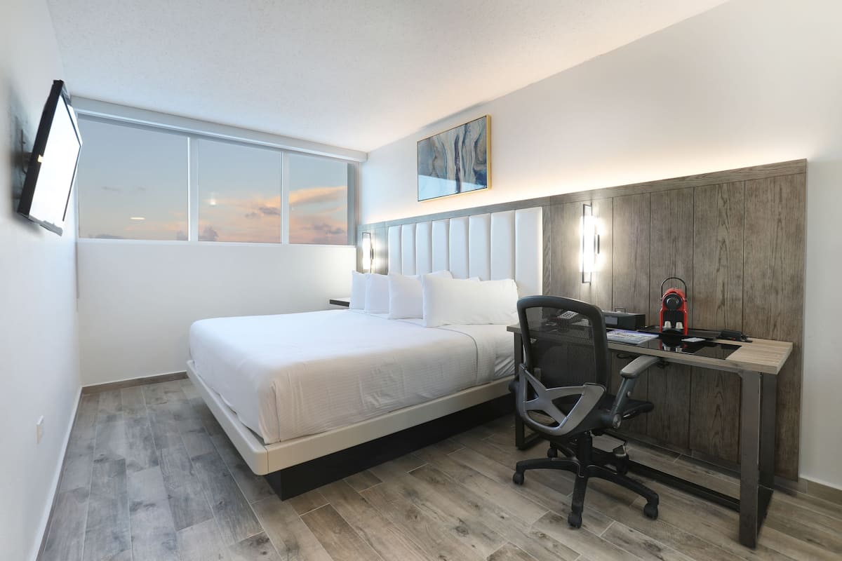 Un dormitorio moderno con cama, escritorio, silla y un amplio ventanal.
