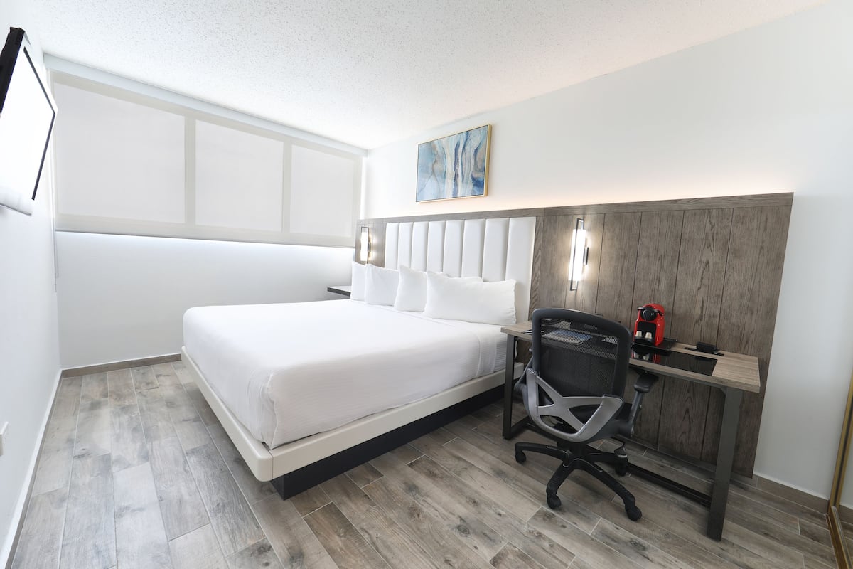 Una habitación de hotel moderna con una cama grande, un escritorio con silla y un cuadro en la pared.