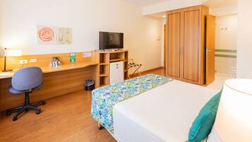 Ein Hotelzimmer mit Bett, Schreibtisch, Stuhl, Fernseher, Kleiderschrank und kleinem Kühlschrank.