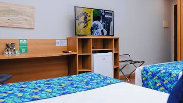 A hotel room with two beds, a television, a small refrigerator, and a wooden shelf.