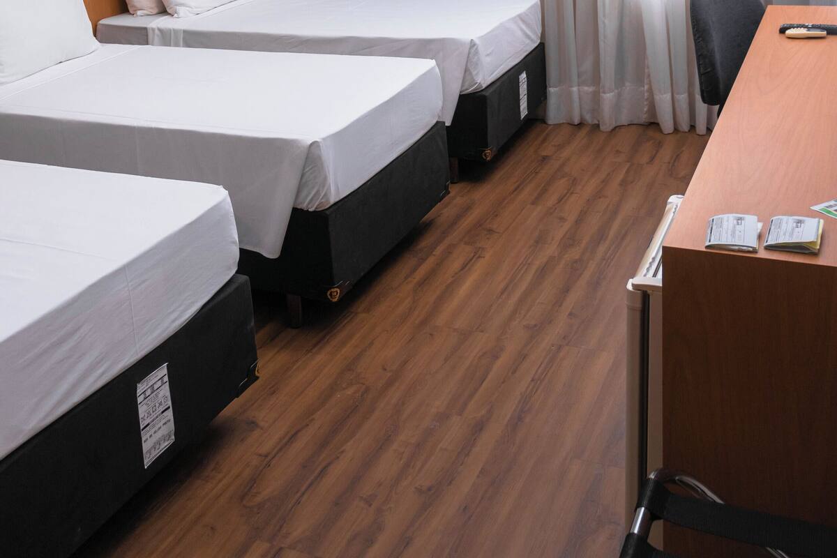 A hotel room with two beds, a desk, a chair, an air conditioning unit, and a large window with curtains.