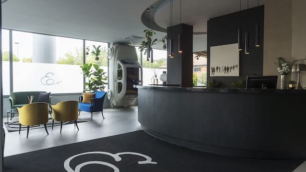 A modern reception area with a curved desk, seating with cushions, and a large window offering a view of greenery. - Elizabeth Lifestyle Hotel (Bologna)