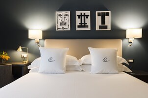 Habitación de hotel con una cama grande, dos mesitas de noche y lámparas fijadas a la pared.