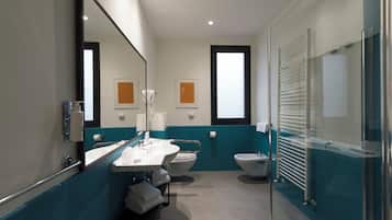 A modern bathroom with a sink, toilet, and bidet, featuring a glass shower enclosure and teal accents.