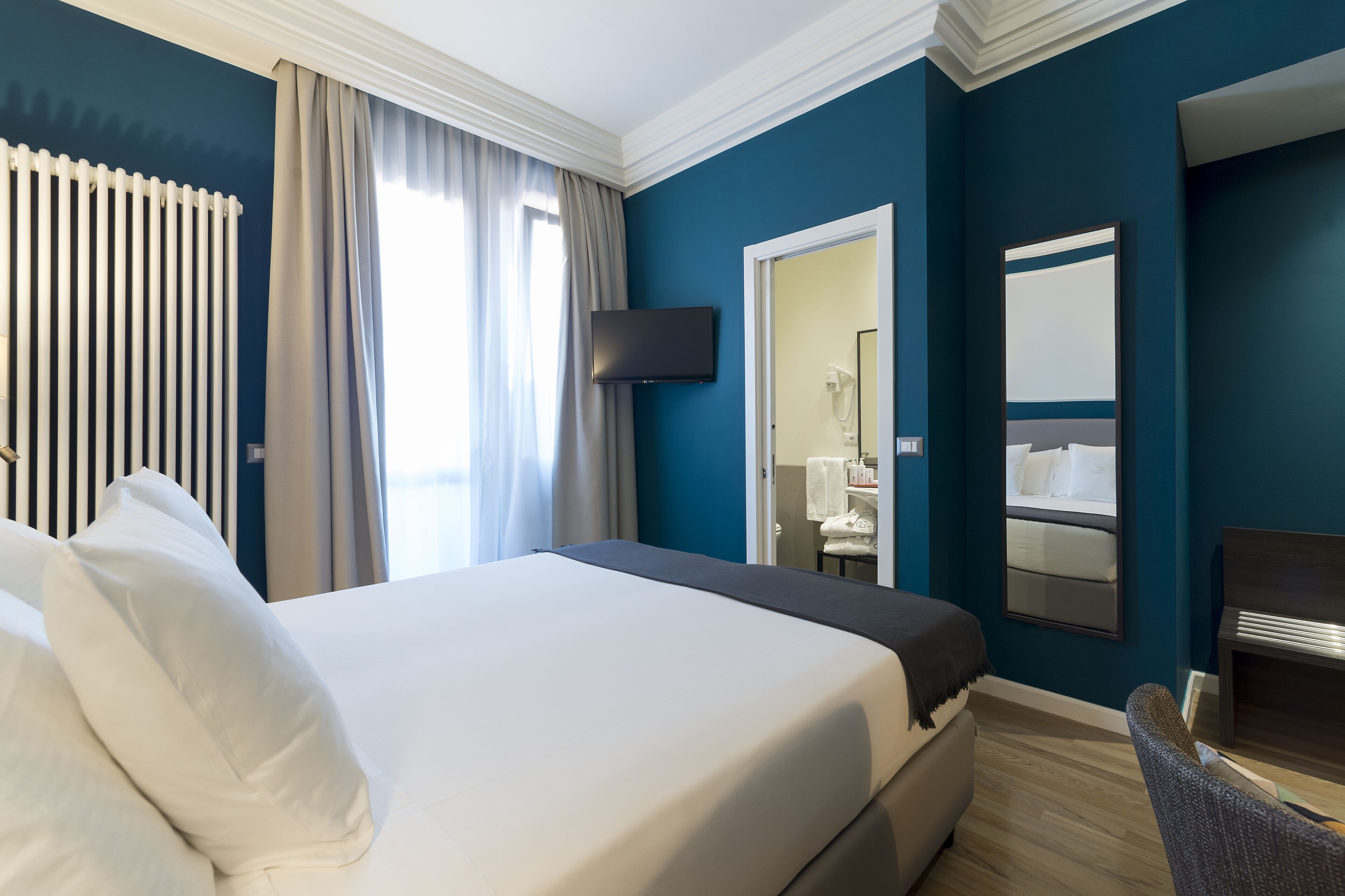 Camera d'albergo con un letto grande, una TV a muro, uno specchio e vista sul bagno.
