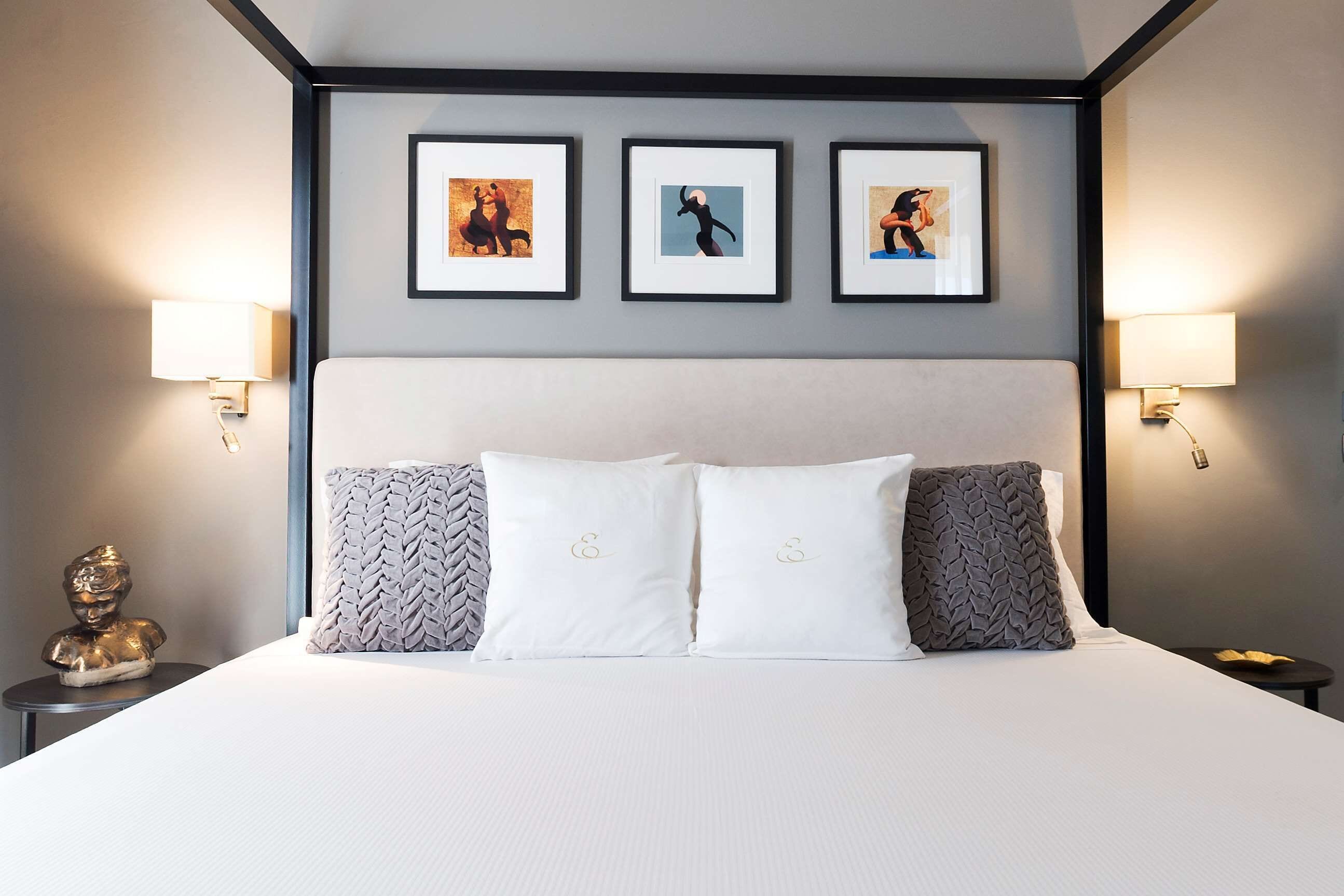 A hotel room with a large bed, two bedside lamps, and three framed pictures on the wall.
