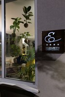 Placa do Hotel Elizabeth Lifestyle, com interior moderno visível através de uma janela, incluindo plantas em vasos e móveis contemporâneos.