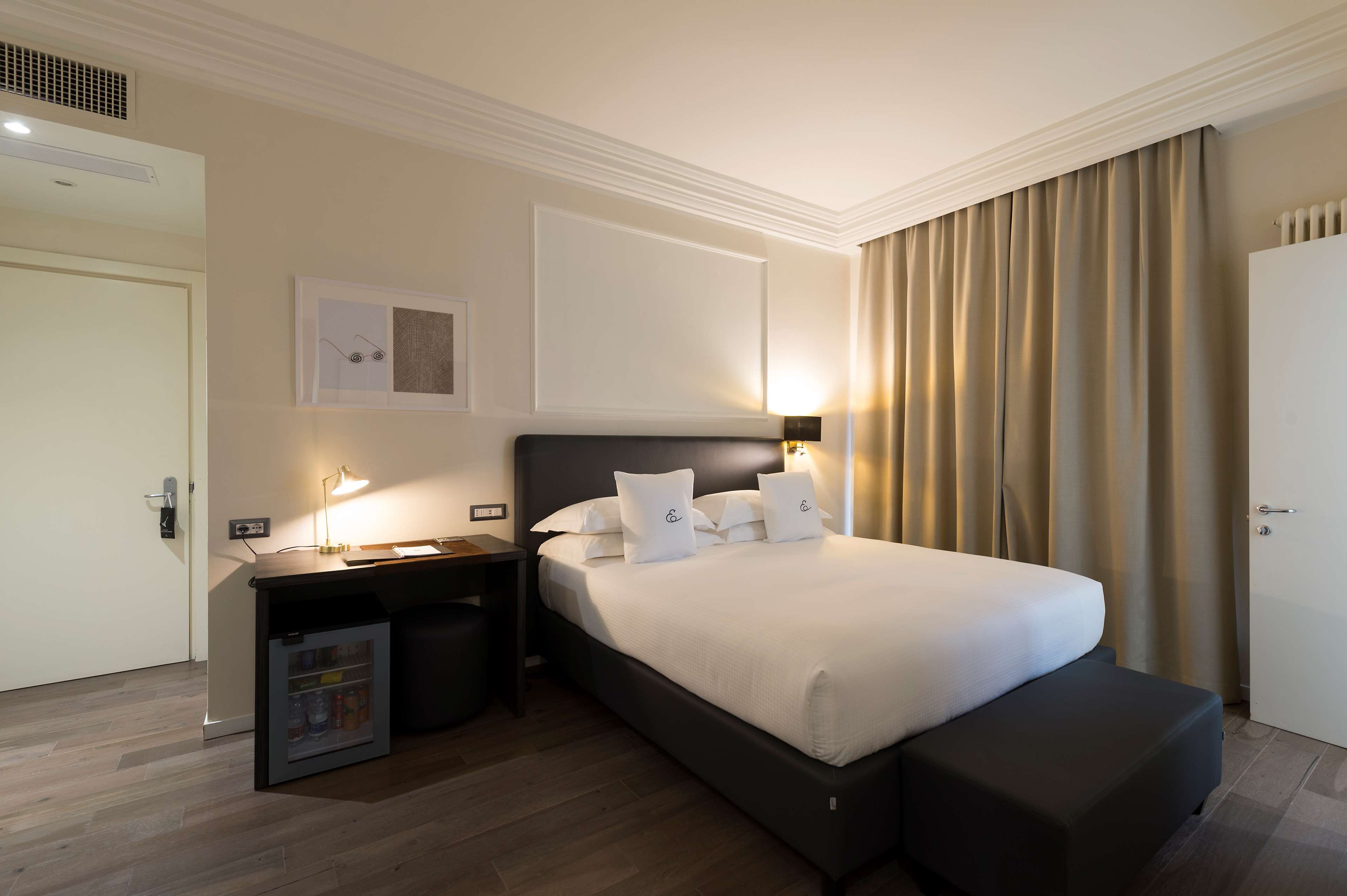 Ein Hotelzimmer mit einem Bett, Nachttischen, einem Schreibtisch und einer Minibar.