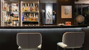 A bar area with shelves of liquor bottles, two upholstered chairs, and a decorative wall piece. - Elizabeth Lifestyle Hotel (Bologna)