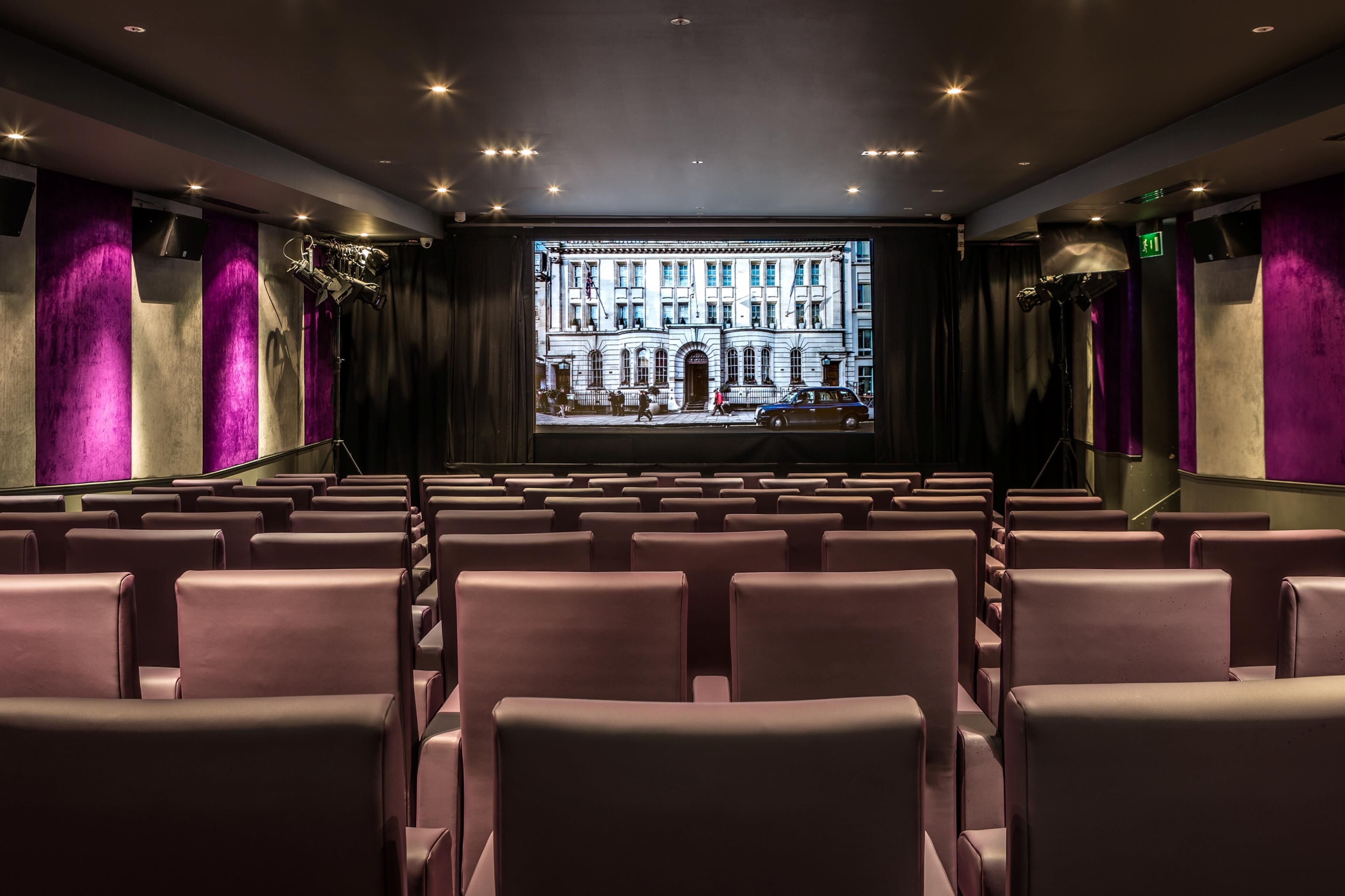 A theater with rows of seats, a large screen, and purple curtains.