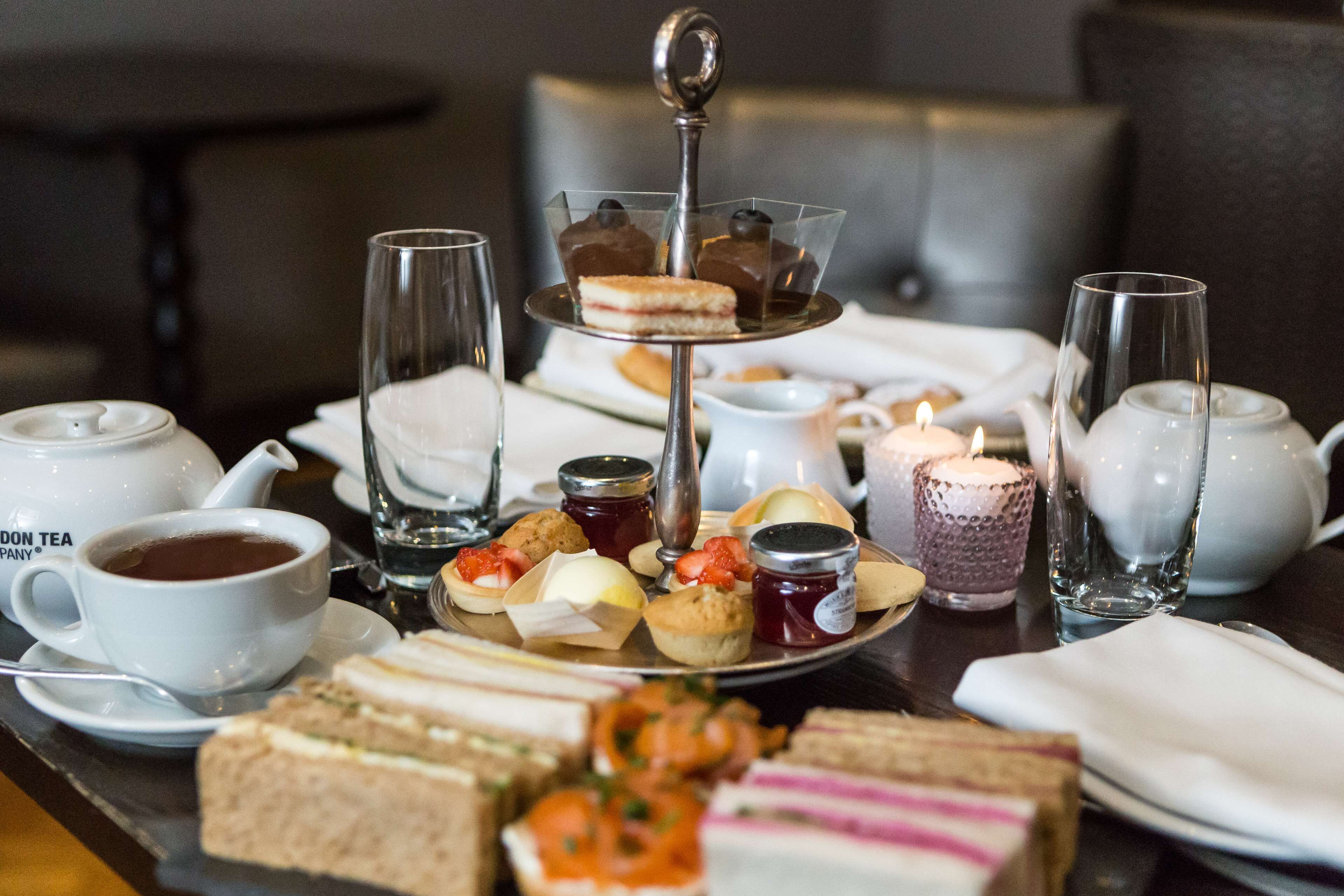 Una mesa con tazas de té, una tetera, un pastelero de varios niveles y diversos bocadillos y pasteles.