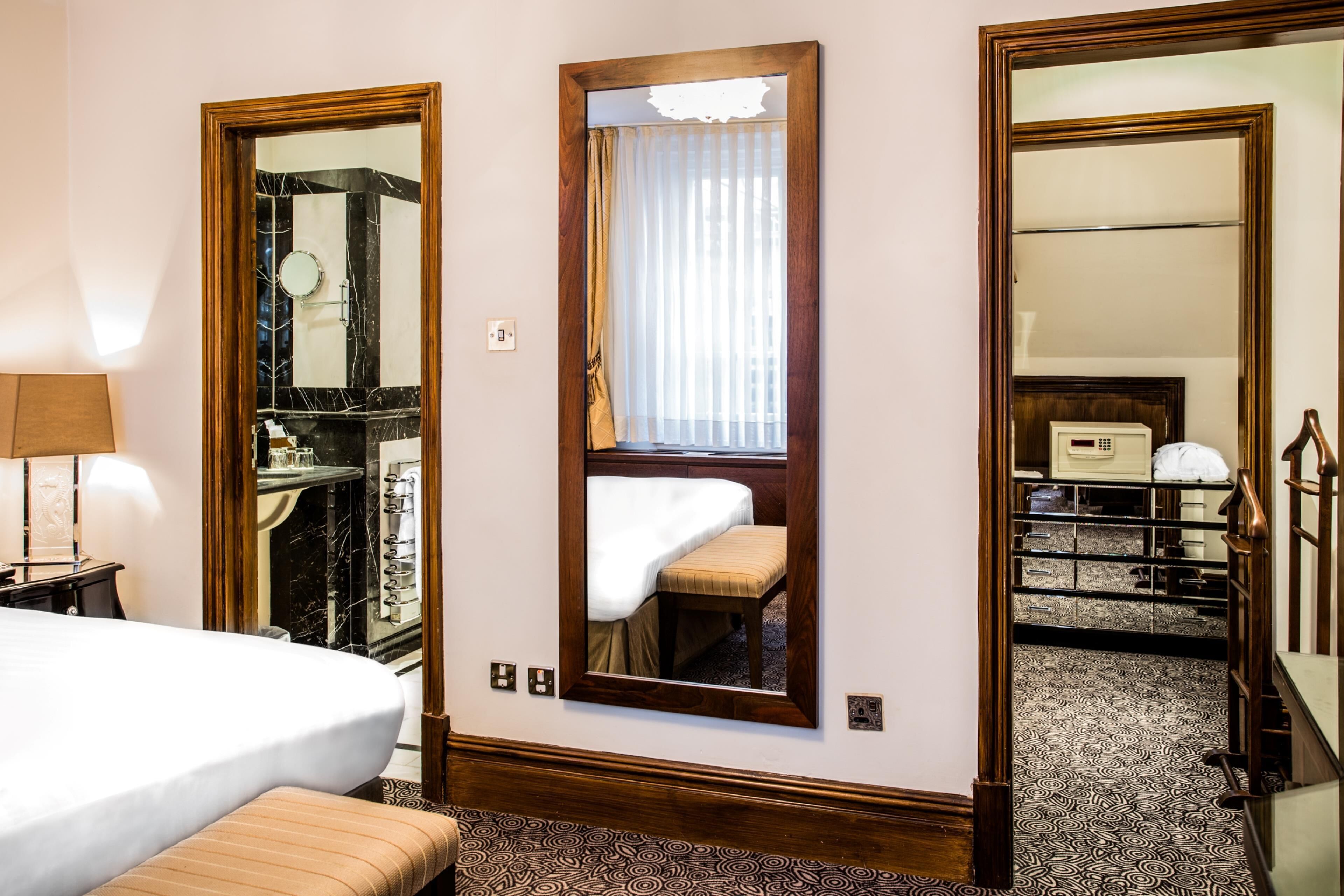 A hotel room with a bed, a mirror, a bedside table, and a wardrobe.