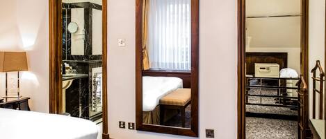 A hotel room with a bed, a mirror, a bedside table, and a wardrobe.