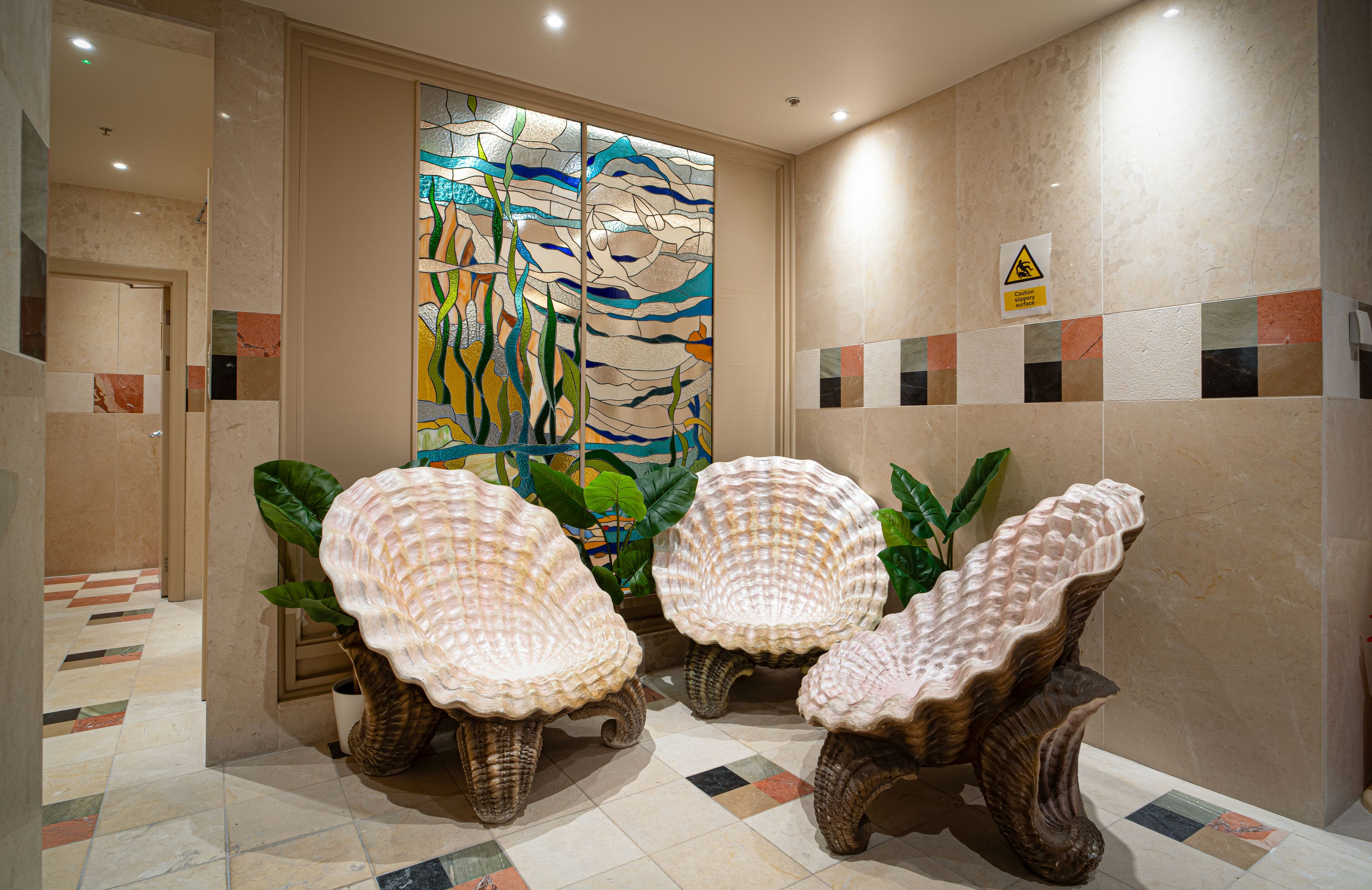 A lobby with a mosaic wall, a warning sign, and three wicker chairs.