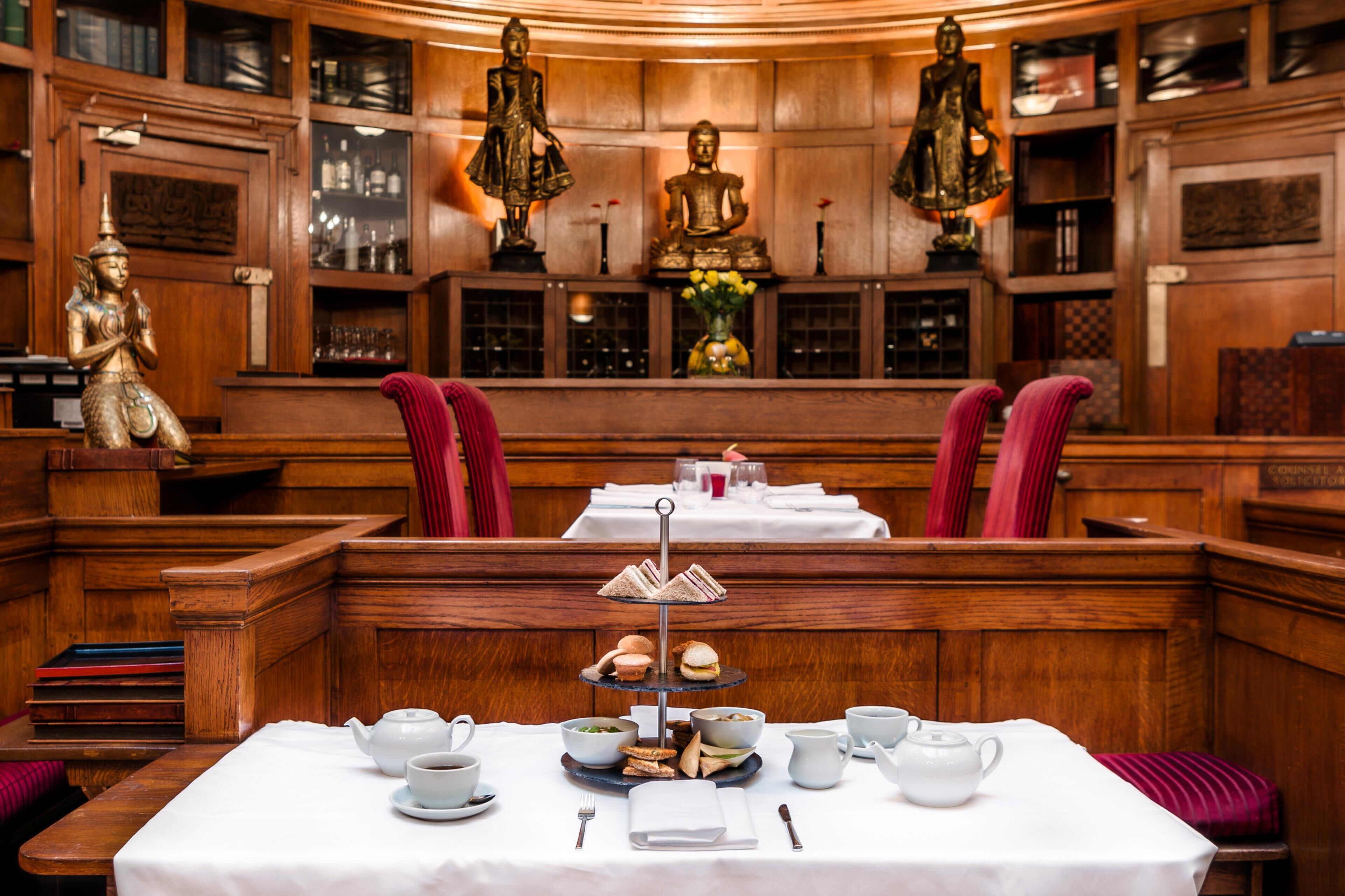 A room with a table set for tea service, wooden paneling, and Buddha statues.